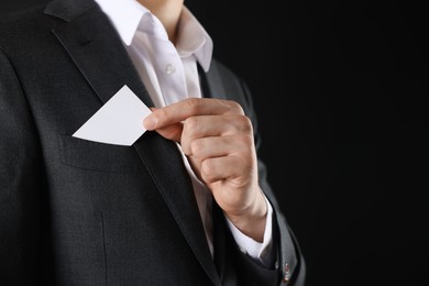 Photo of Man taking blank business card from pocket of his jacket on black background, closeup. Mockup for design