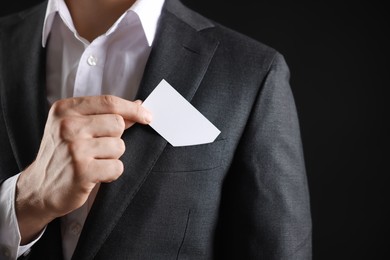 Photo of Man taking blank business card from pocket of his jacket on black background, closeup. Mockup for design