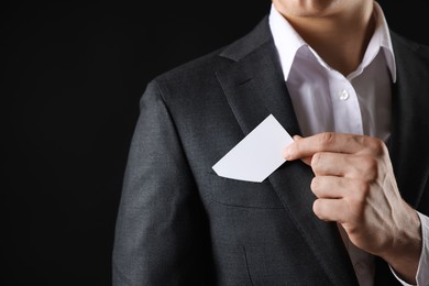 Photo of Man taking blank business card from pocket of his jacket on black background, closeup. Mockup for design