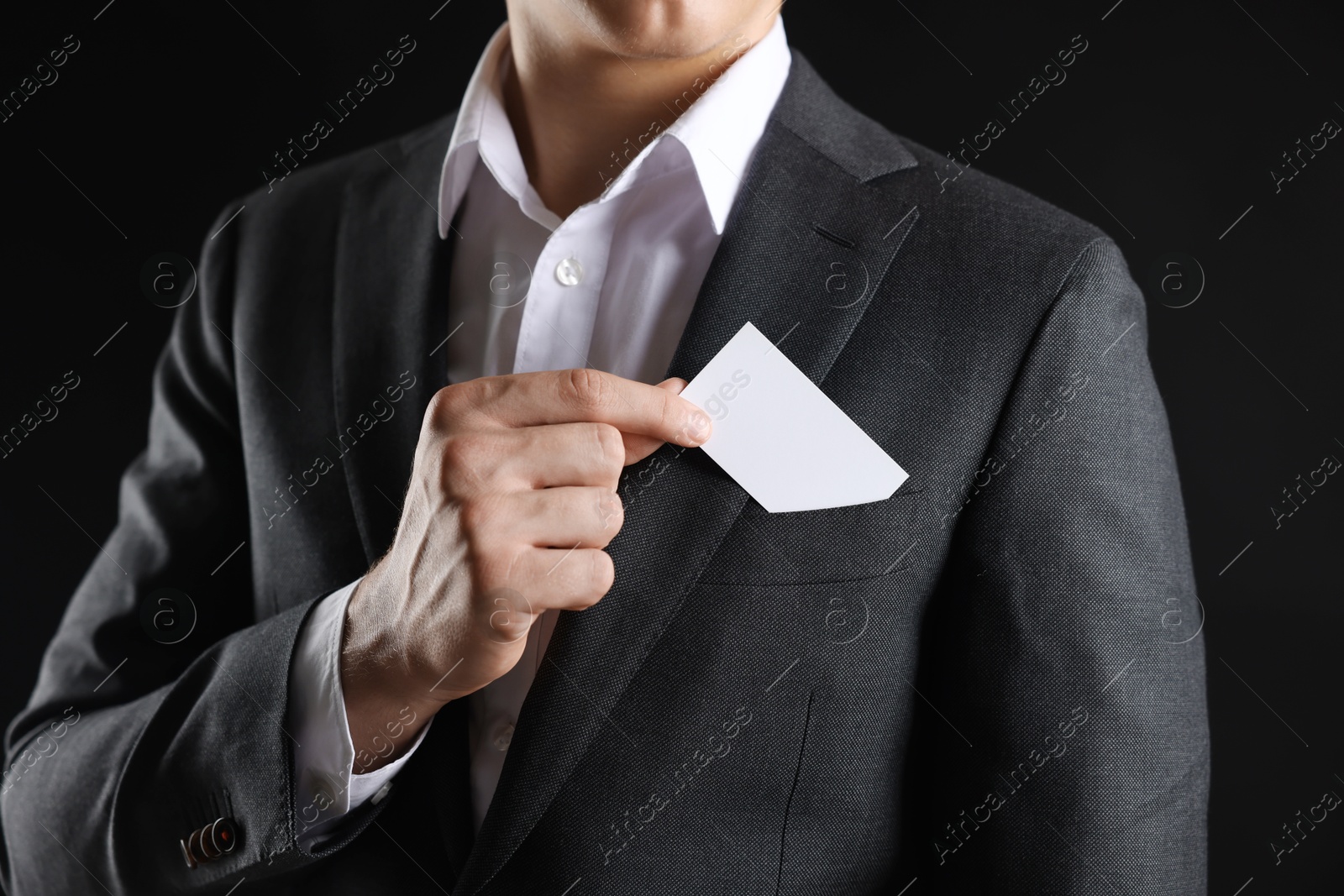 Photo of Man taking blank business card from pocket of his jacket on black background, closeup. Mockup for design