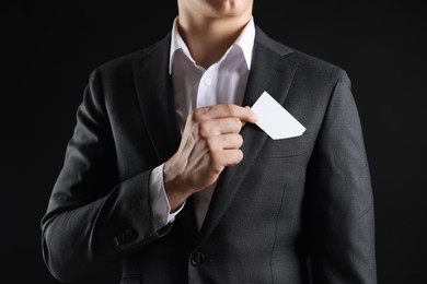 Photo of Man taking blank business card from pocket of his jacket on black background, closeup. Mockup for design