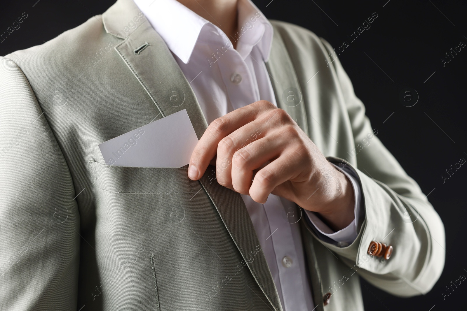 Photo of Man taking blank business card from pocket of his jacket on black background, closeup. Mockup for design