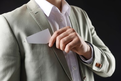 Photo of Man taking blank business card from pocket of his jacket on black background, closeup. Mockup for design