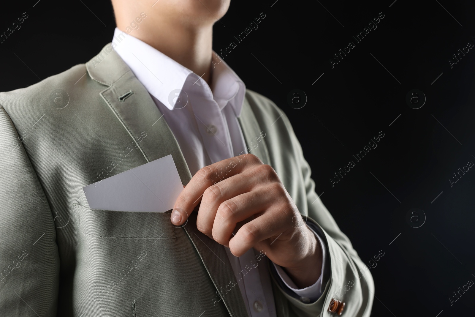 Photo of Man taking blank business card from pocket of his jacket on black background, closeup. Mockup for design