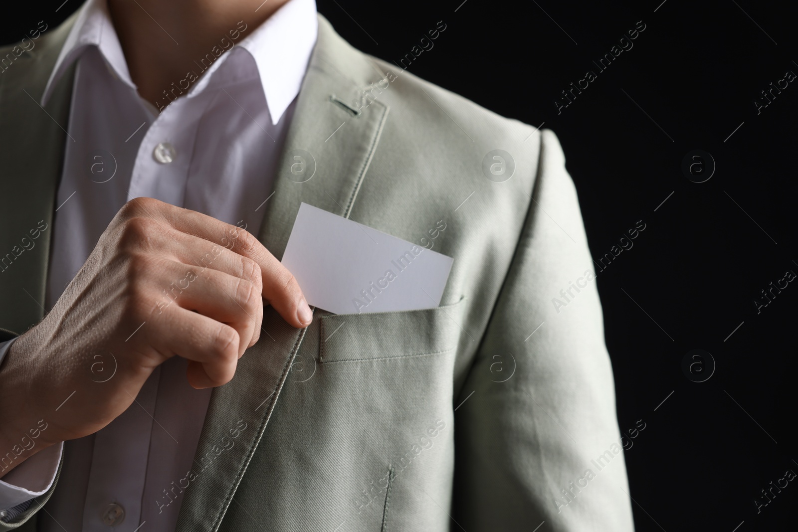 Photo of Man taking blank business card from pocket of his jacket on black background, closeup. Mockup for design