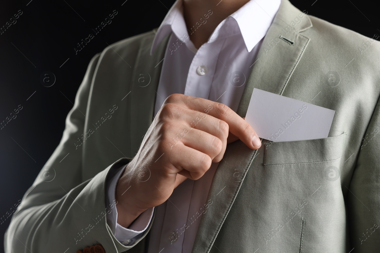 Photo of Man taking blank business card from pocket of his jacket on black background, closeup. Mockup for design