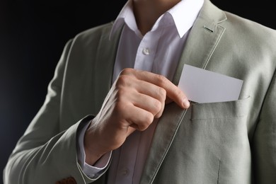 Photo of Man taking blank business card from pocket of his jacket on black background, closeup. Mockup for design