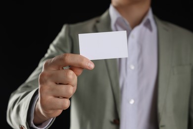 Man holding blank business card on black background, closeup. Mockup for design