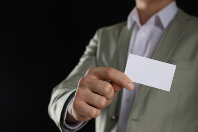 Man holding blank business card on black background, closeup. Mockup for design