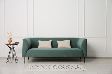 Photo of Stylish sofa, pillows and side table with decor near white wall indoors