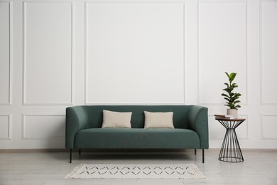 Photo of Stylish sofa, pillows and side table with houseplant near white wall indoors