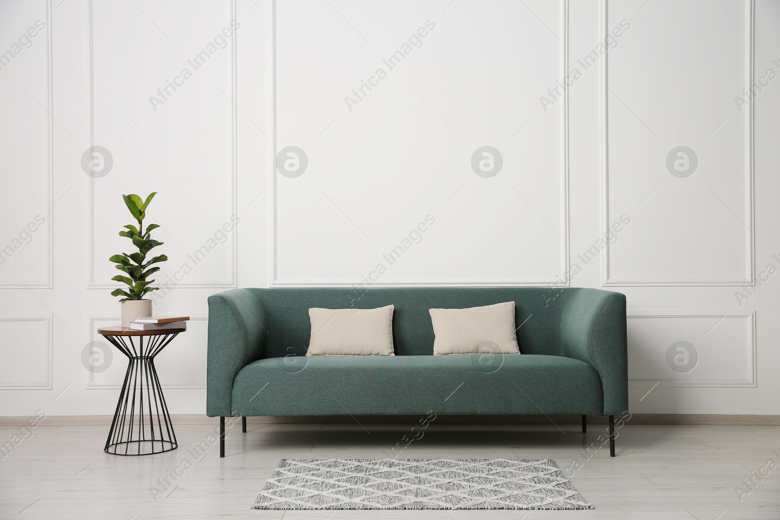 Photo of Stylish sofa, pillows and side table with houseplant near white wall indoors