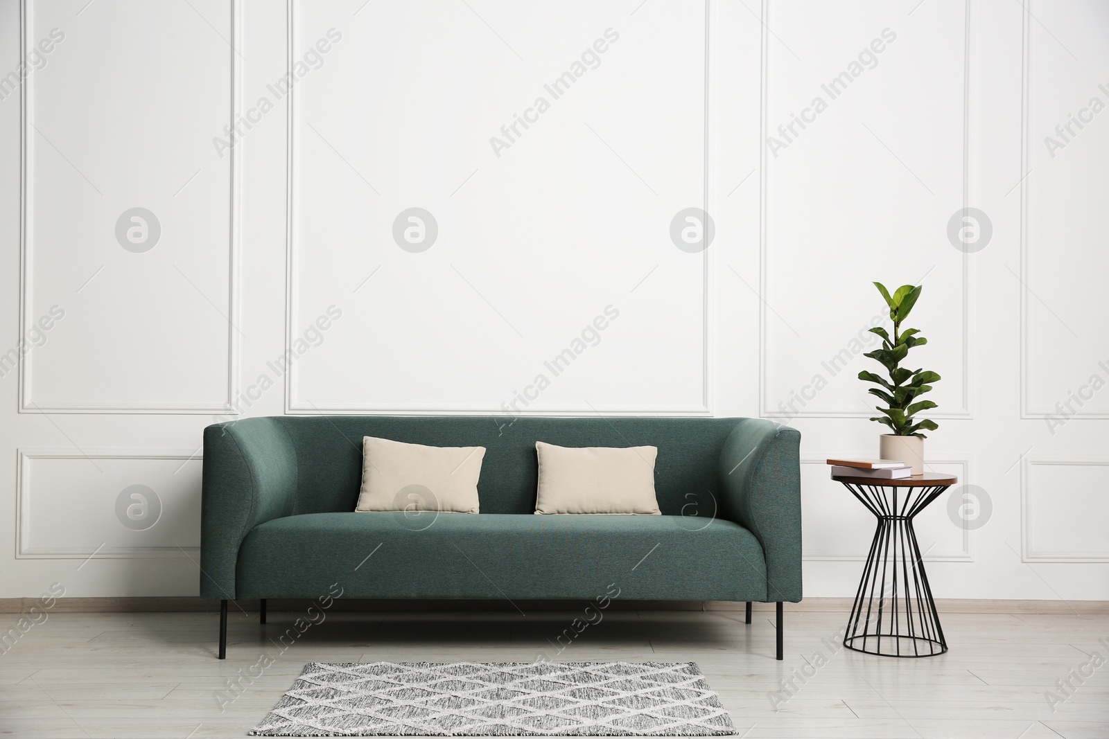 Photo of Stylish sofa, pillows and side table with houseplant near white wall indoors