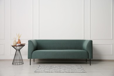 Photo of Stylish sofa and side table with decor near white wall indoors