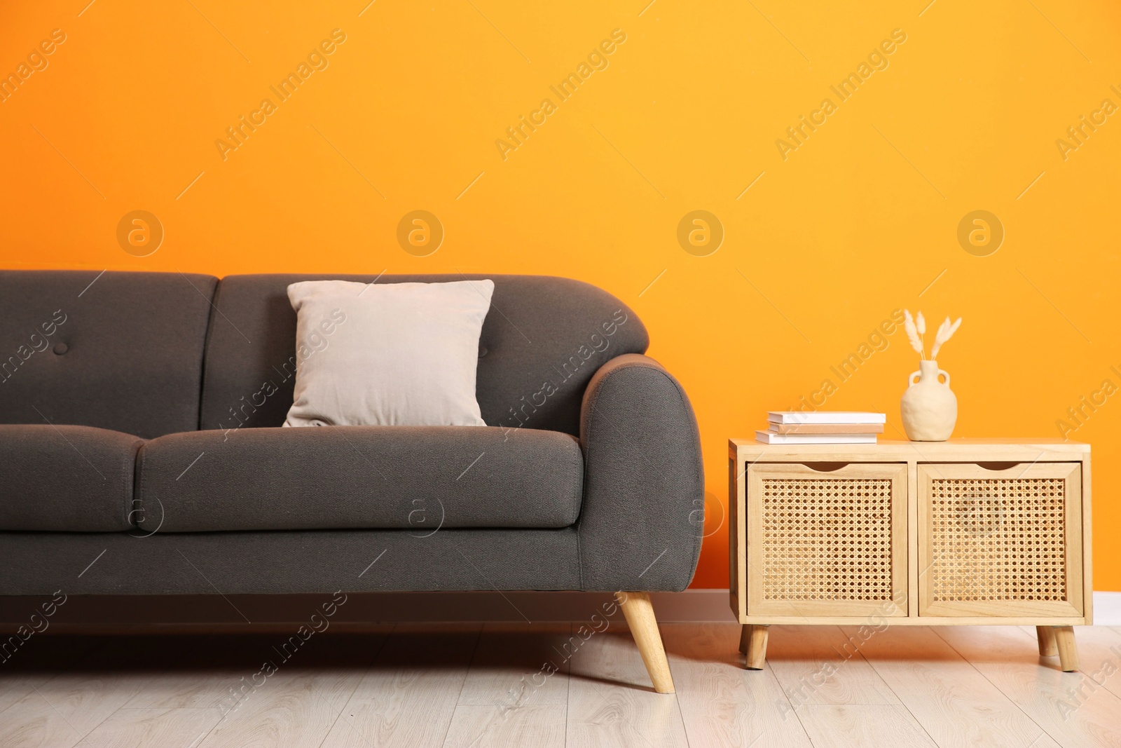 Photo of Stylish sofa, pillow and storage cabinet with decor near orange wall indoors