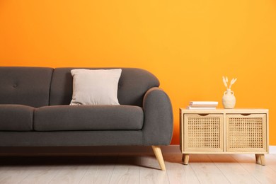 Photo of Stylish sofa, pillow and storage cabinet with decor near orange wall indoors