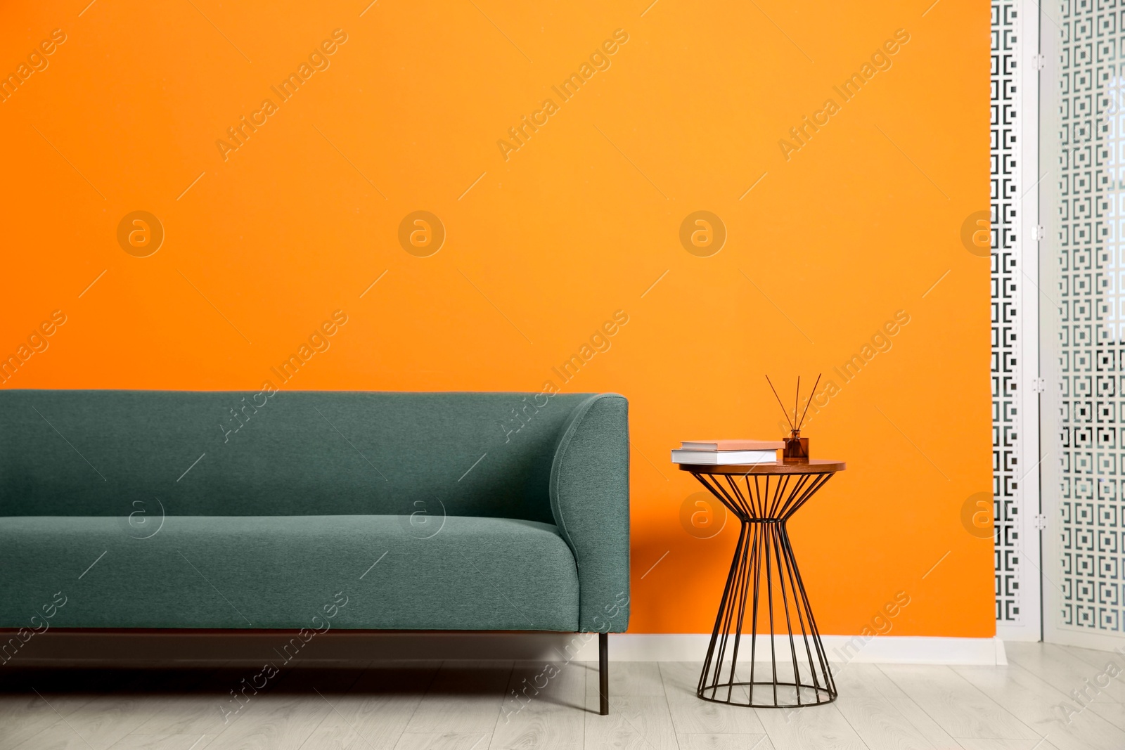 Photo of Stylish sofa and side table with decor near orange wall indoors