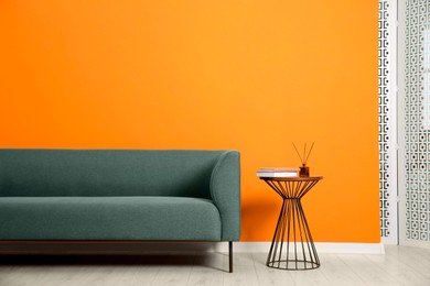 Photo of Stylish sofa and side table with decor near orange wall indoors