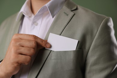 Man taking blank business card from pocket of his jacket on green background, closeup. Mockup for design