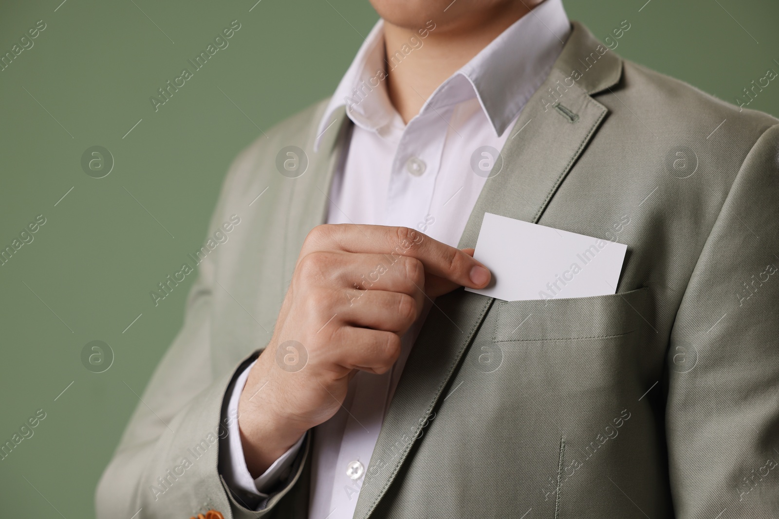 Photo of Man taking blank business card from pocket of his jacket on green background, closeup. Mockup for design