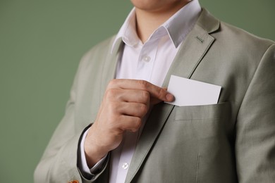 Man taking blank business card from pocket of his jacket on green background, closeup. Mockup for design