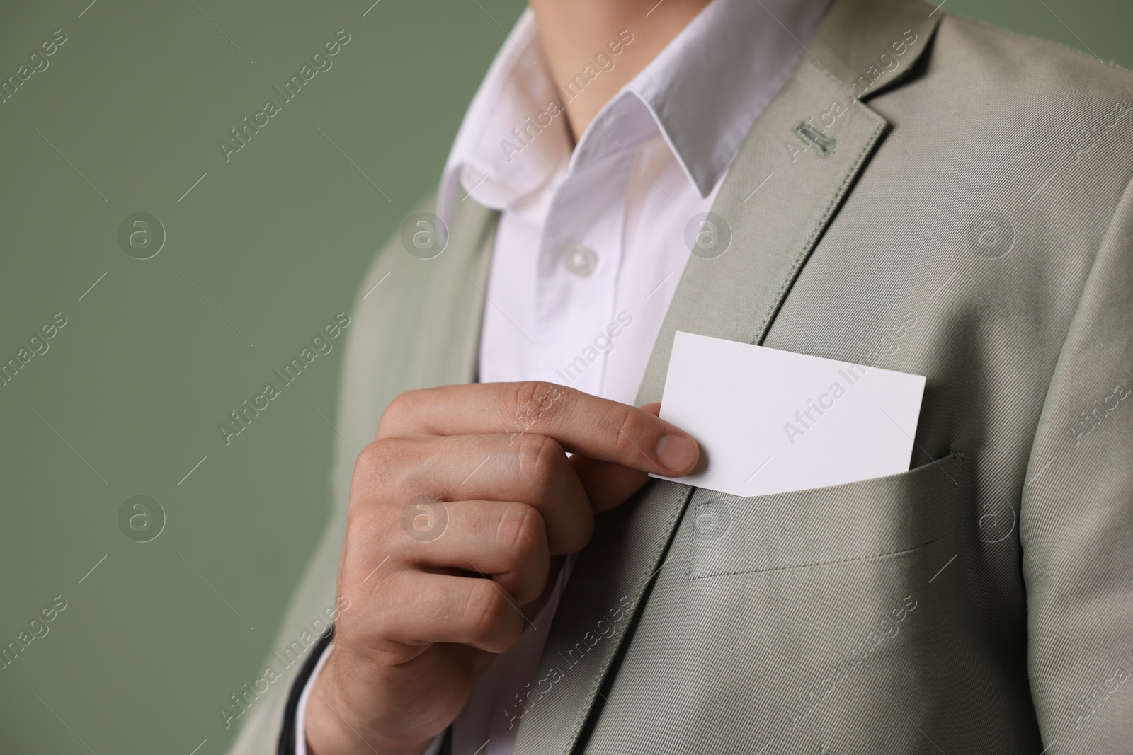 Photo of Man taking blank business card from pocket of his jacket on green background, closeup. Mockup for design