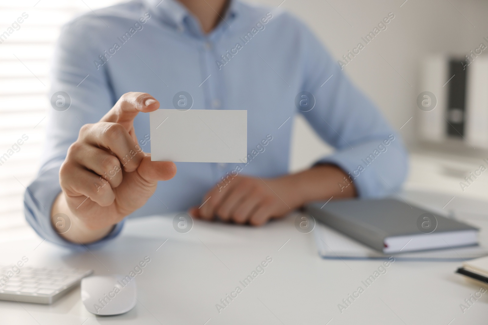 Photo of Woman holding blank business card at table in office, closeup. Mockup for design