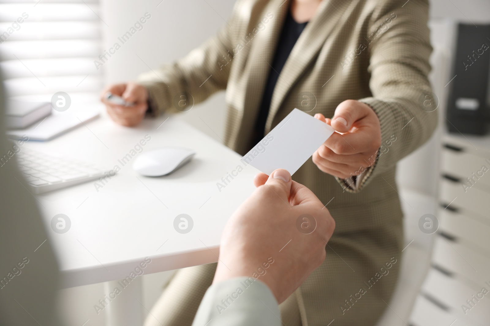 Photo of Woman giving business card to man at table in office, closeup. Mockup for design