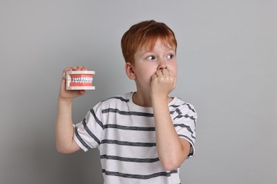 Dental phobia. Scared boy with model of jaw on grey background