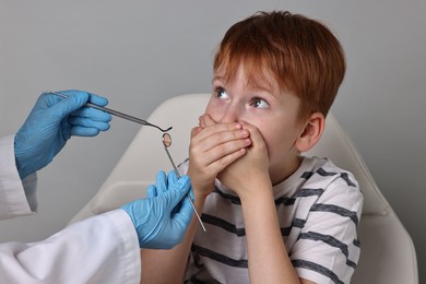 Photo of Dental phobia. Dentist working with scared little boy on grey background