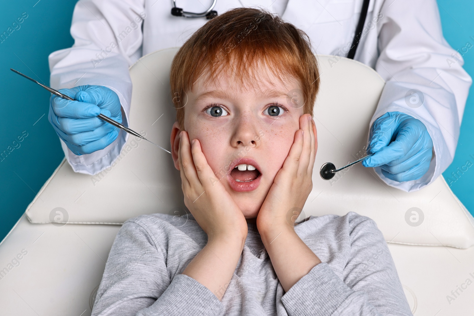 Photo of Dental phobia. Dentist working with scared little boy on light blue background