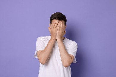 Portrait of scared young man on violet background