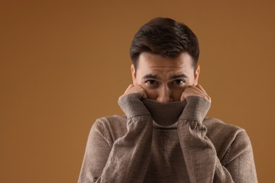 Portrait of scared young man on brown background, space for text