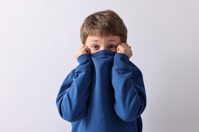 Scared little boy hiding on light background