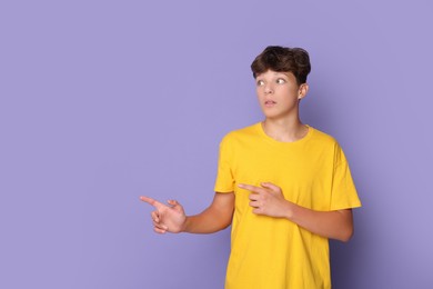 Photo of Scared teenage boy pointing at something on violet background. Space for text