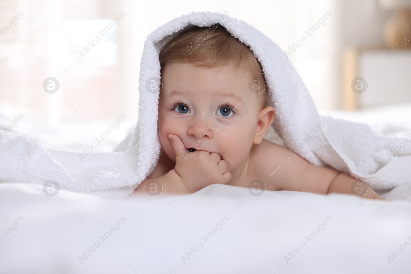 Photo of Cute baby under terry towel lying on bed at home