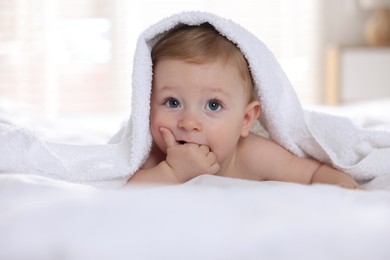 Cute baby under terry towel lying on bed at home