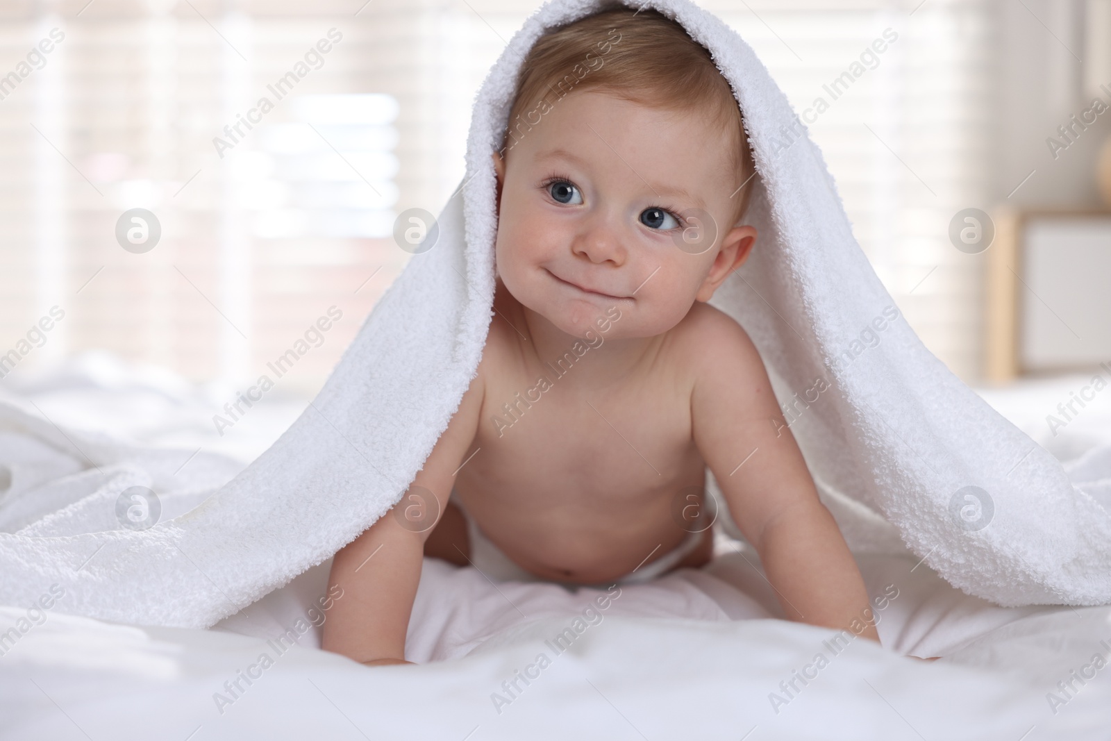 Photo of Cute baby under terry towel lying on bed at home