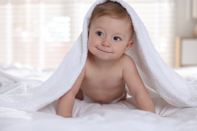 Cute baby under terry towel lying on bed at home