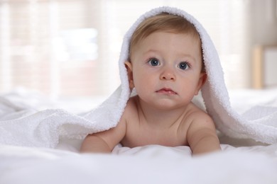 Photo of Cute baby under terry towel lying on bed at home