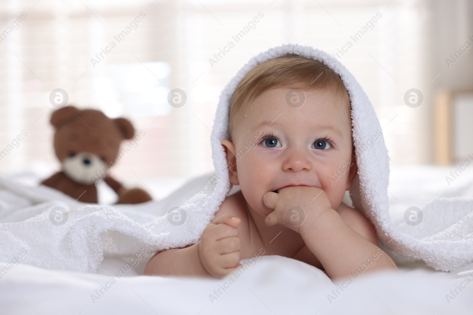 Photo of Cute baby under terry towel lying on bed at home