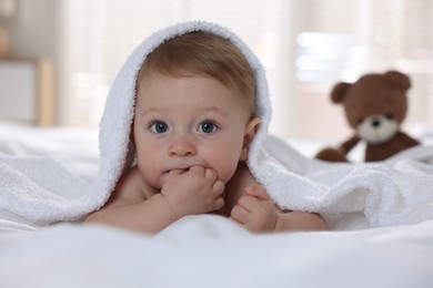 Photo of Cute baby under terry towel lying on bed at home