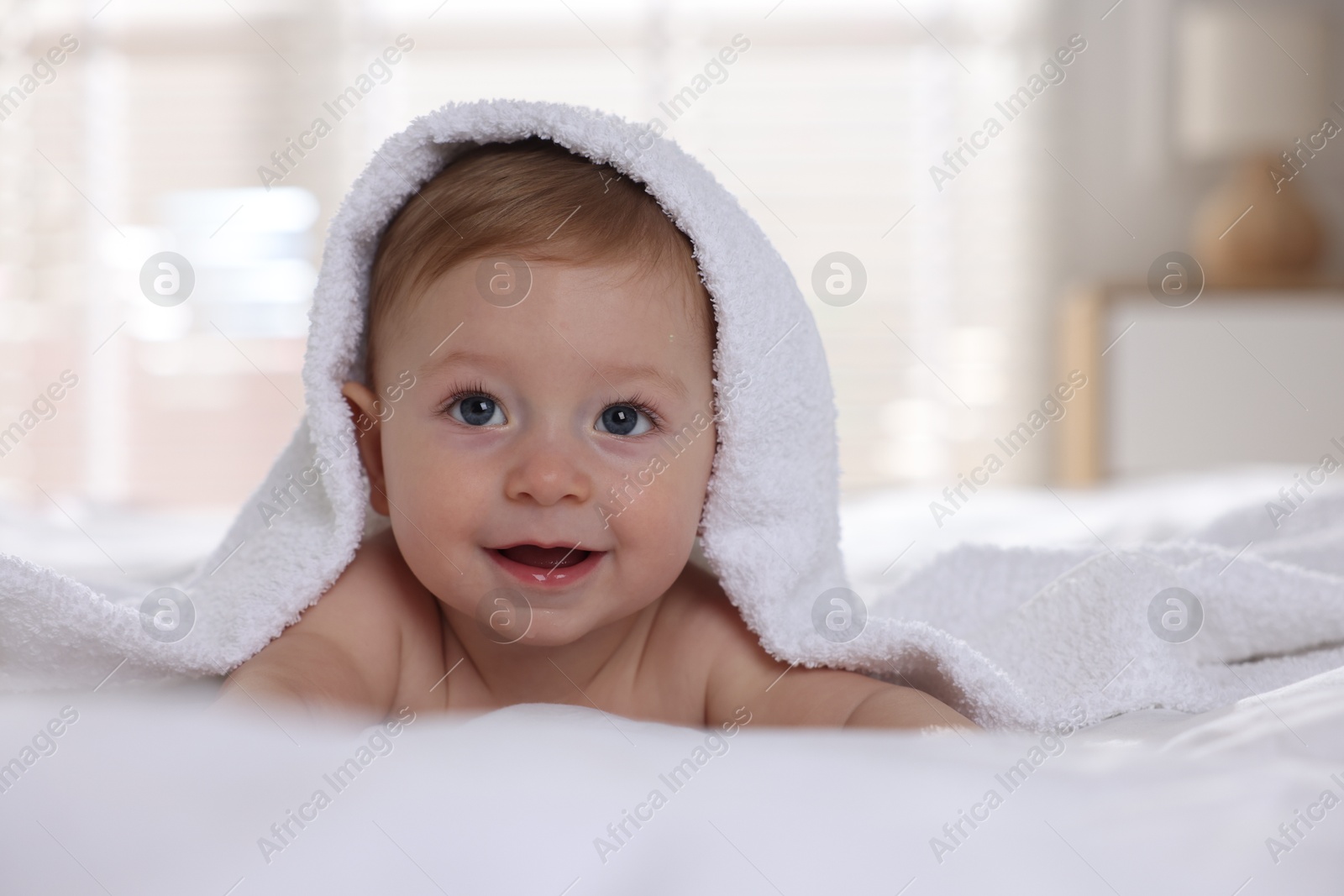 Photo of Cute baby under terry towel lying on bed at home