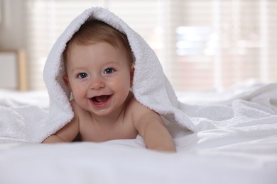 Photo of Cute baby under terry towel lying on bed at home