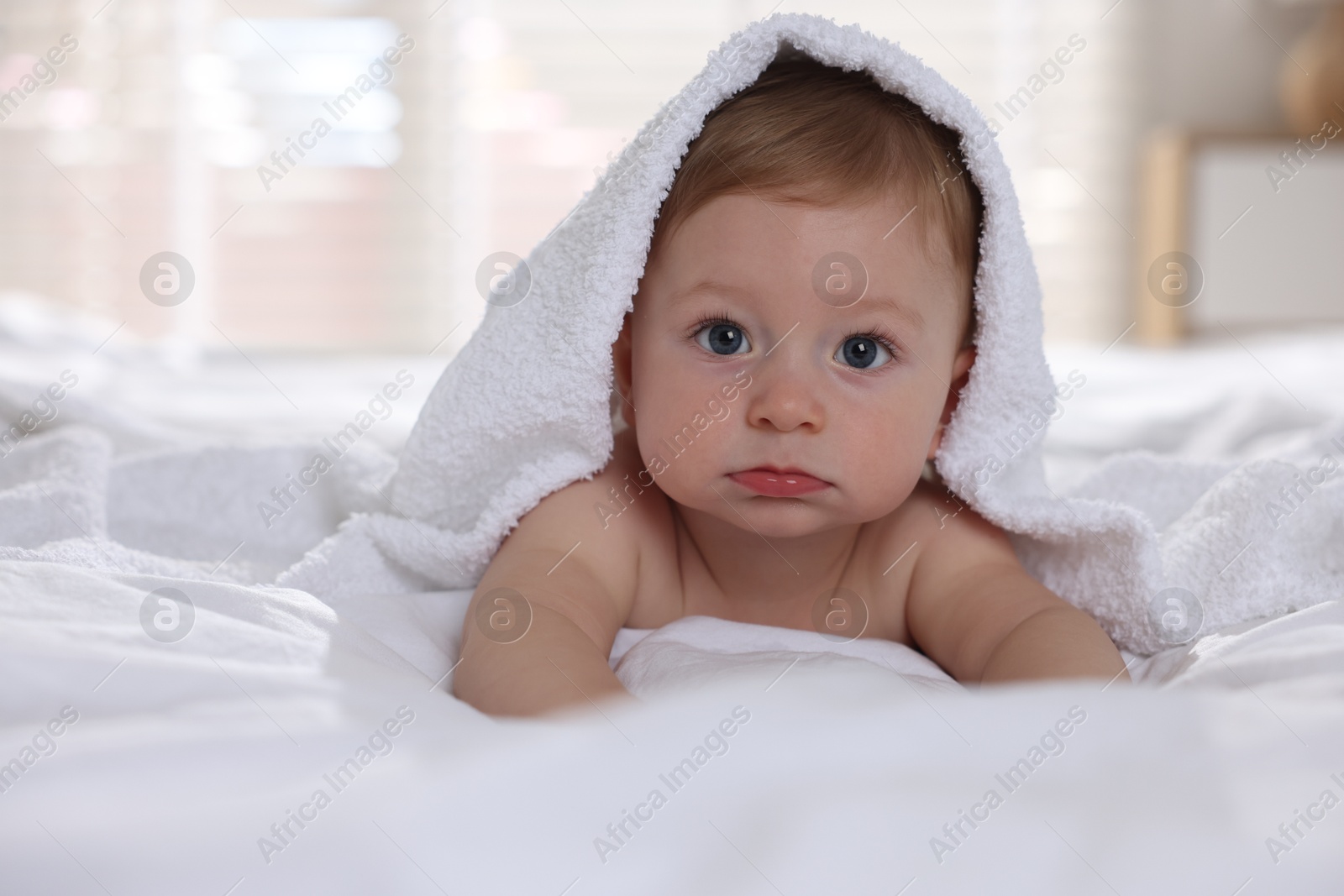 Photo of Cute baby under terry towel lying on bed at home