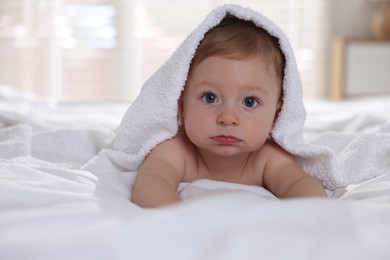 Cute baby under terry towel lying on bed at home