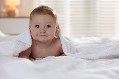 Cute baby under terry towel lying on bed at home