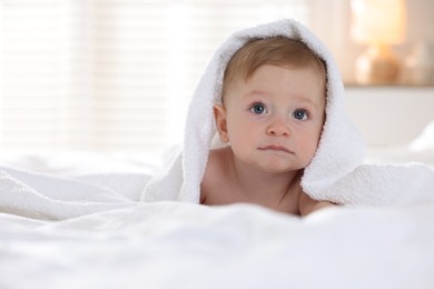 Cute baby under terry towel lying on bed at home