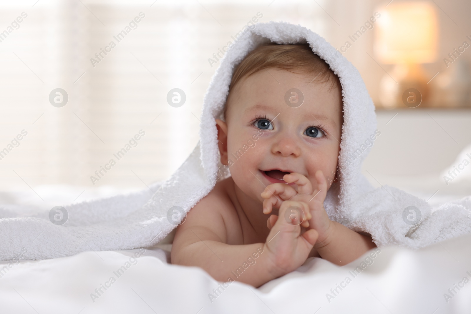 Photo of Cute baby under terry towel lying on bed at home