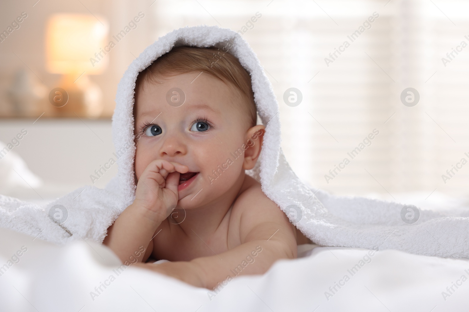 Photo of Cute baby under terry towel lying on bed at home